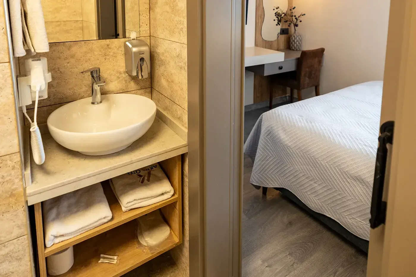 Classic Oda banyosu: travertin dokulu seramik, çanak lavabo ve ahşap rafta Aktaş Otel havluları
