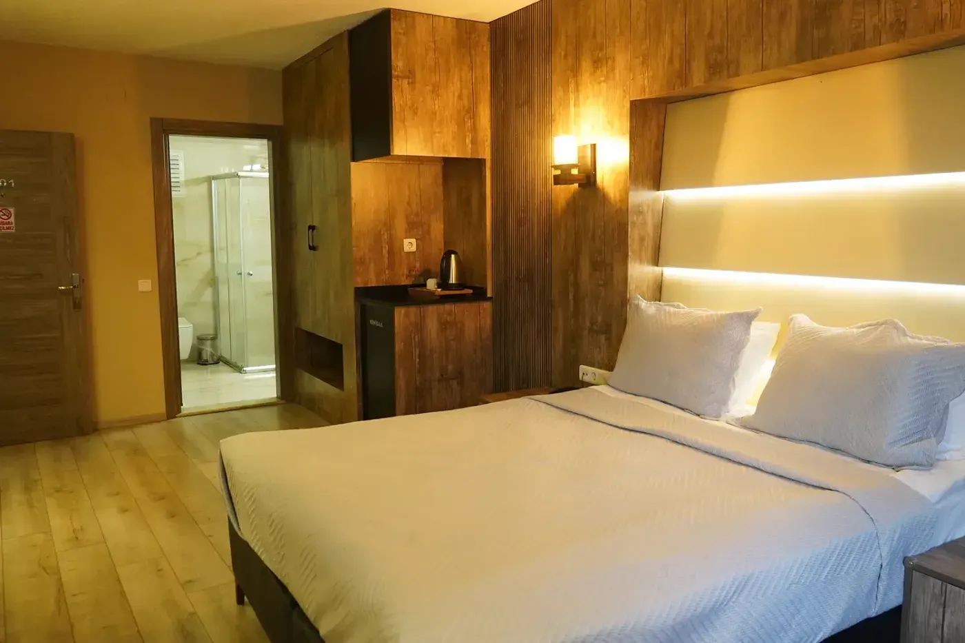 Junior Suit’in giriş tarafı: açık banyo kapısından duşakabin, ahşap gardırop ve minibar nişi
