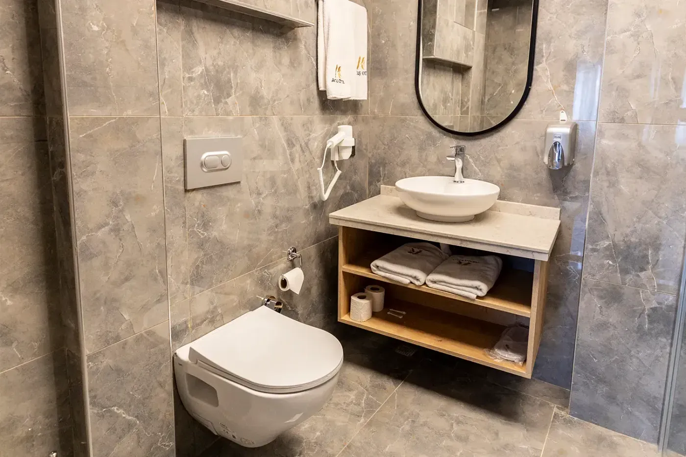 Standart Oda banyosu: gri mermer desenli seramik, asma klozet, çanak lavabo ve Aktaş Otel havluları
