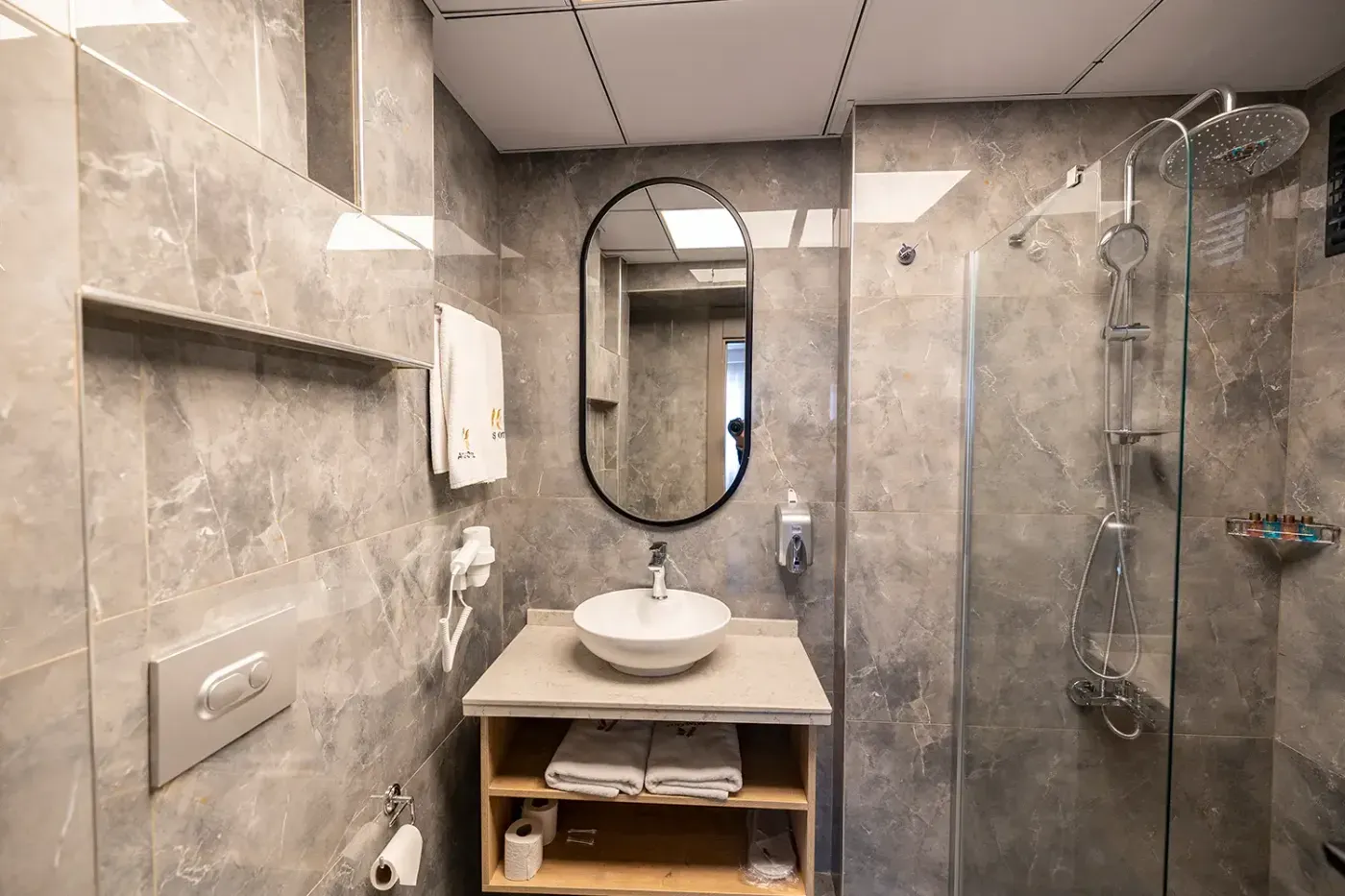 Standart Oda banyosunda tepe duşlu cam duşakabin, çanak lavabo ve oval ayna