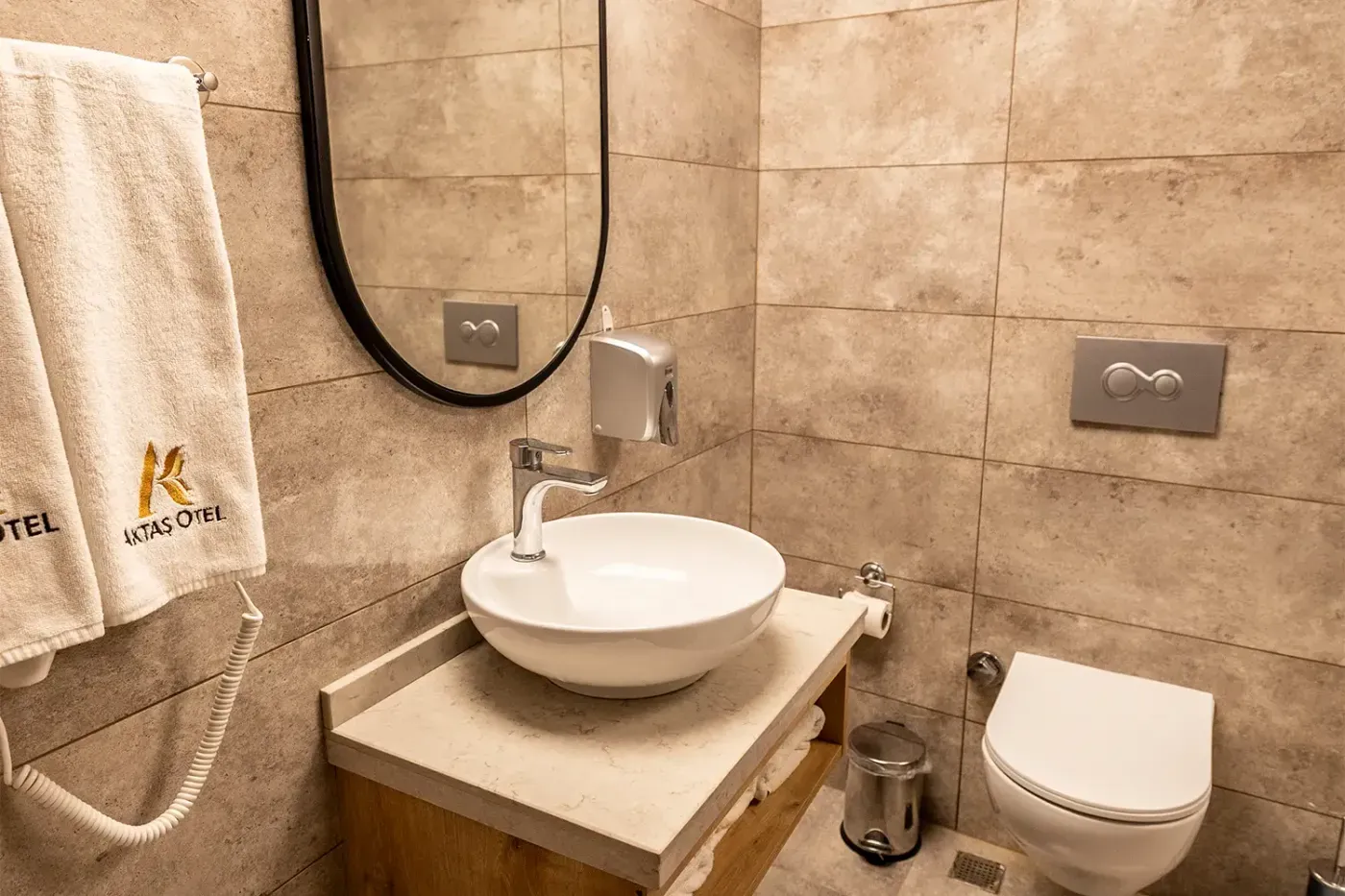 Triple Oda banyosu: çanak lavabo, siyah çerçeveli oval ayna, Aktaş Otel havluları ve saç kurutma makinesi